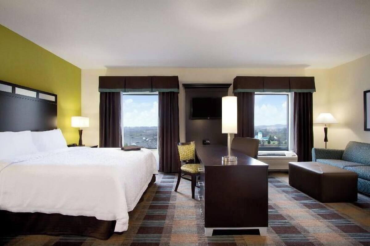 A hotel room with a bed, desk, chair, sofa, and a TV.