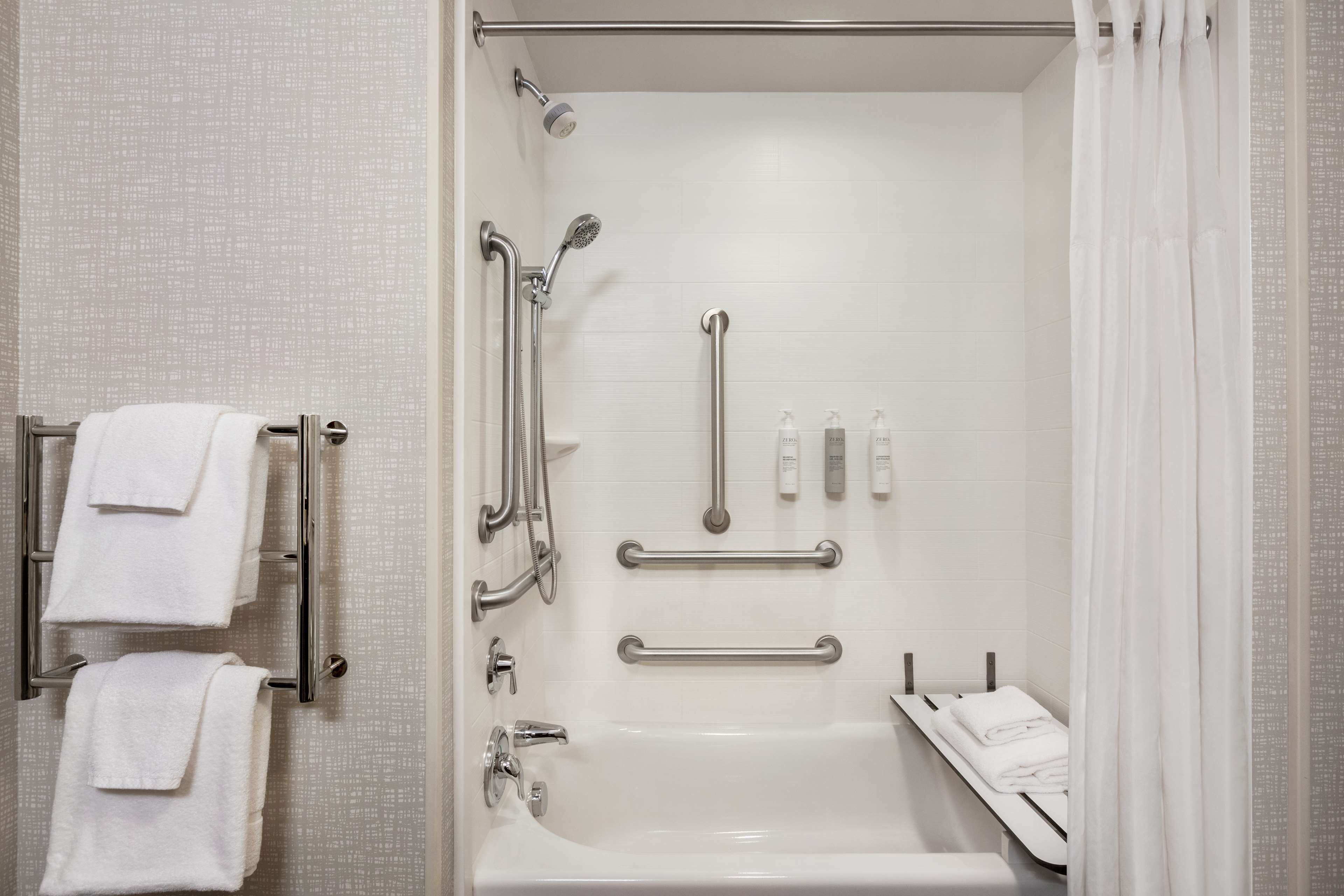A modern bathroom with a bathtub, shower, and handrails.