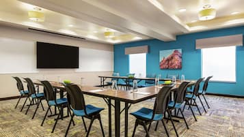 A conference room with a large table, chairs, a projector screen, and a painting on the wall.