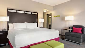 Una habitación de hotel con una cama grande, mesitas de noche, una silla y una pequeña mesa.