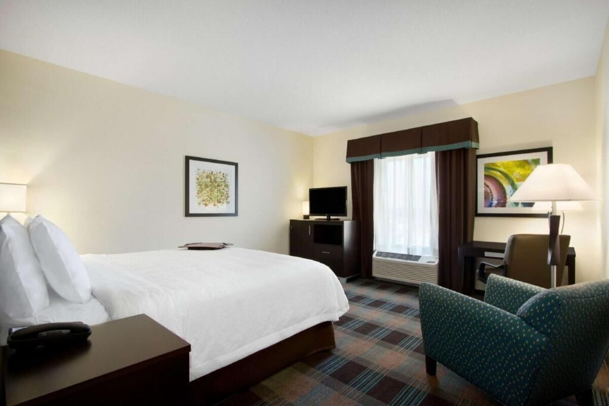 A hotel room with a bed, a desk, a chair, a television, and a window with curtains.