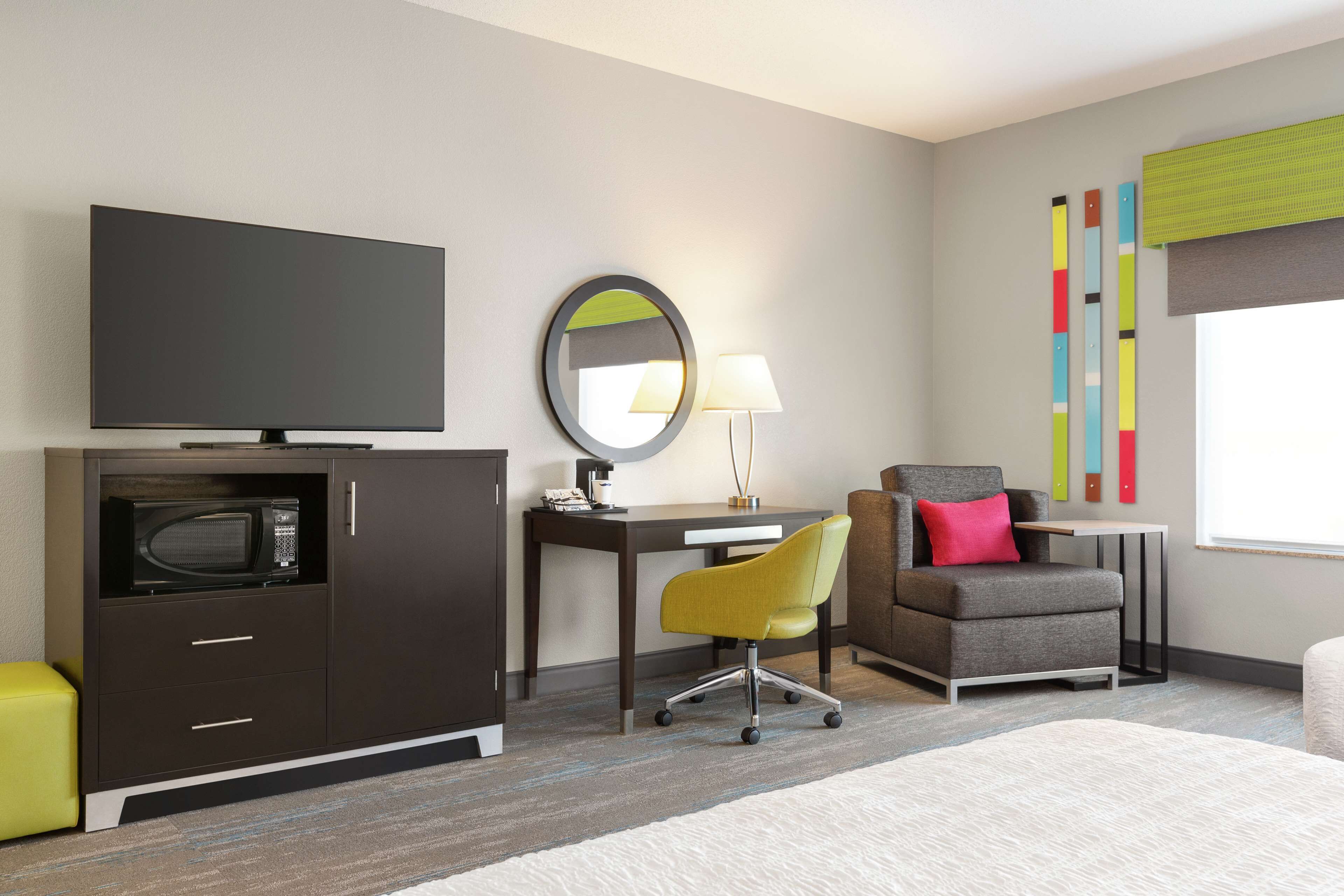 Una habitación de hotel moderna con televisión de pantalla plana, escritorio con lámpara, sillón cómodo, microondas y un pequeño sofá.
