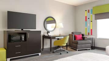 Una habitación de hotel moderna con televisión de pantalla plana, escritorio con lámpara, sillón cómodo, microondas y un pequeño sofá.