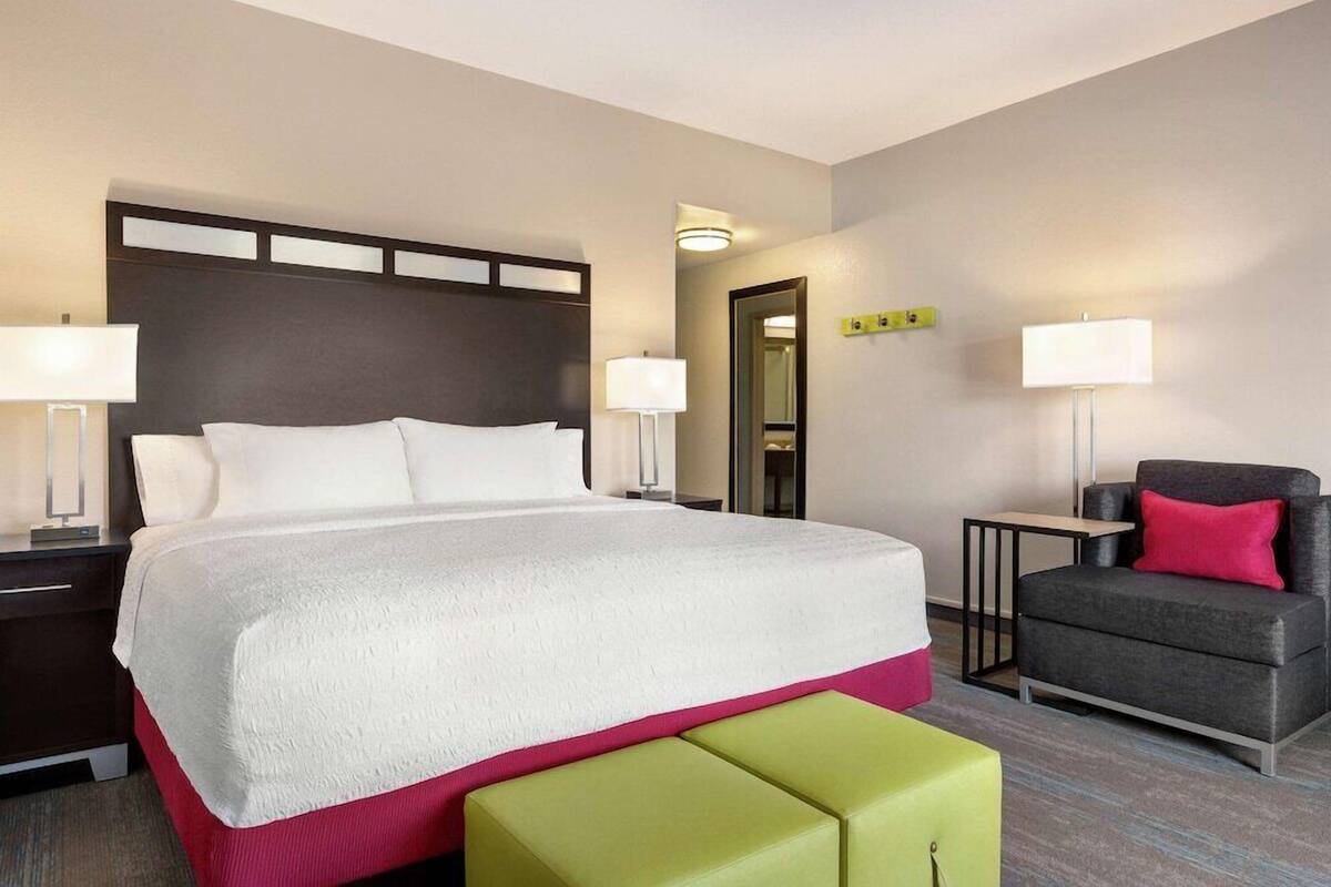 A hotel room with a large bed, bedside tables, a chair, and a small table.