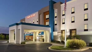 A modern hotel with a 'Welcome' sign, a flag, and a well-lit entrance. - Hampton Inn & Suites York South (York)