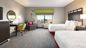 A hotel room with a desk, two beds, a chair, a window with a view, and a mirror. - Hampton Inn & Suites York South (York)