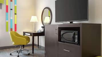 Habitación de hotel con escritorio, una silla amarilla, televisión, microondas, armario y espejo.