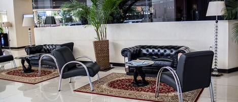 Un hall d’entrée avec deux canapés en cuir noir, une grande plante en pot et un tapis aux motifs rouges et beige.