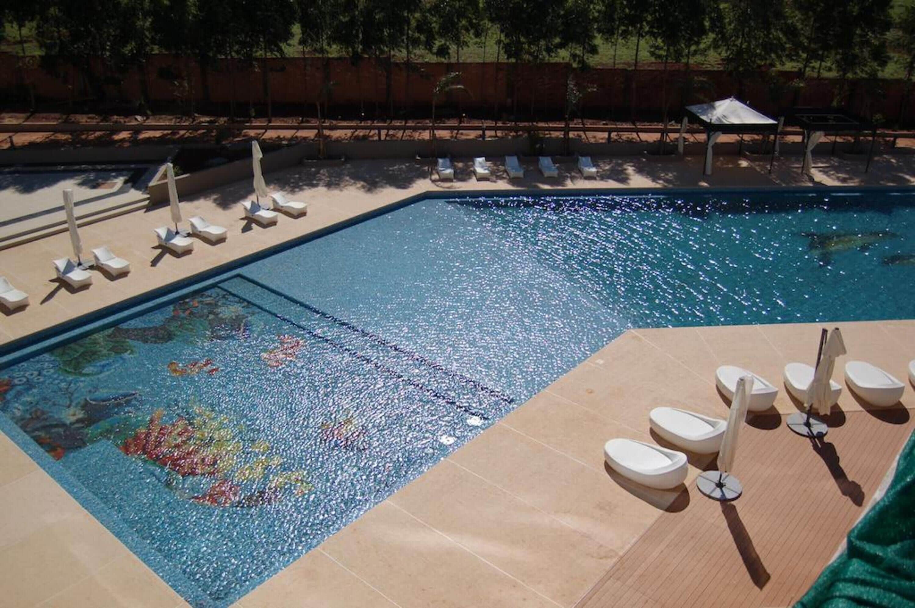 A swimming pool with a mosaic design, lounge chairs, and umbrellas.