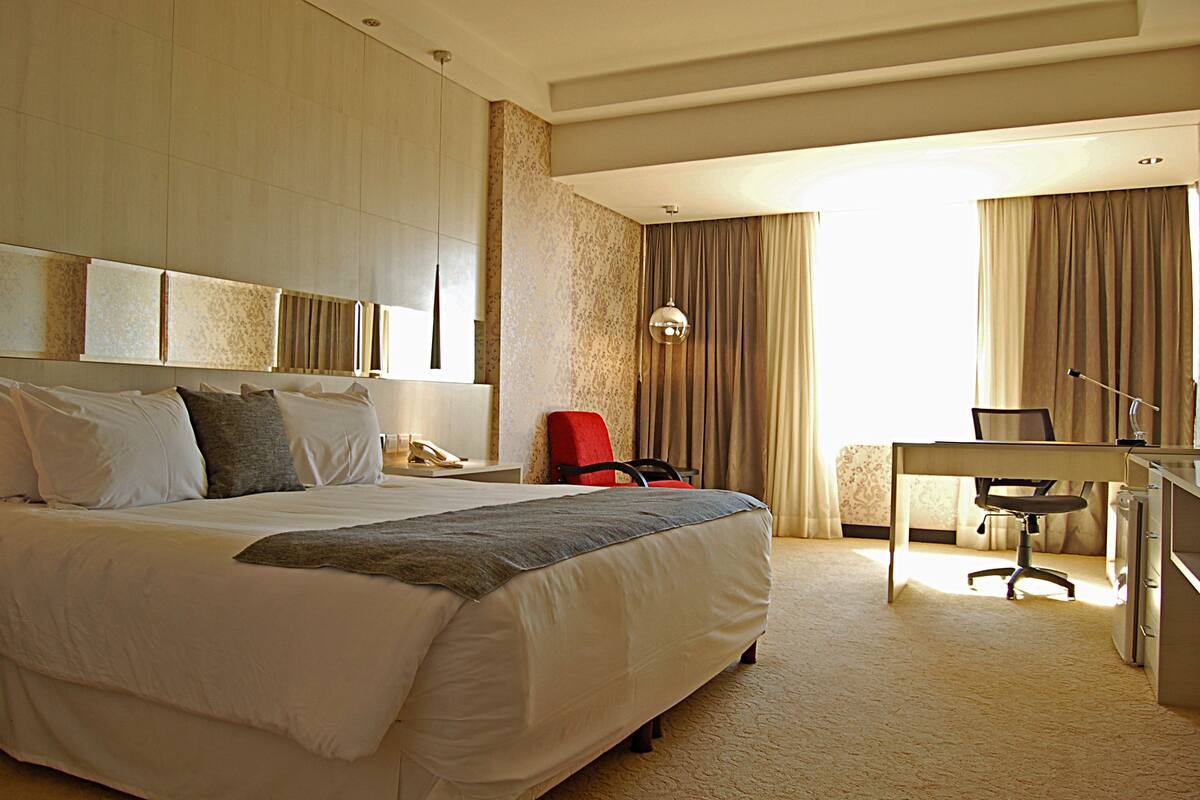 A hotel room with a large bed, a desk, a chair, and a telephone.