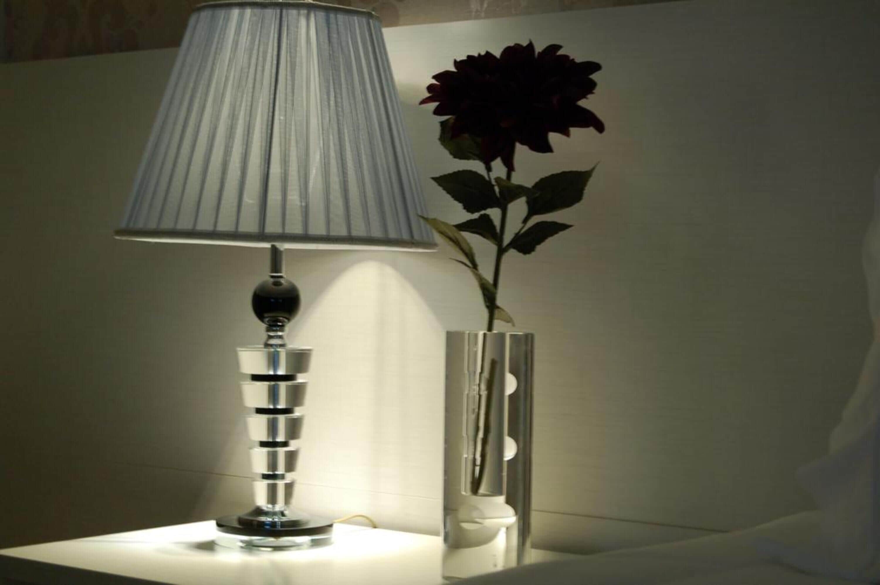 Una lámpara moderna con una pantalla texturizada y un florero con una sola flor.