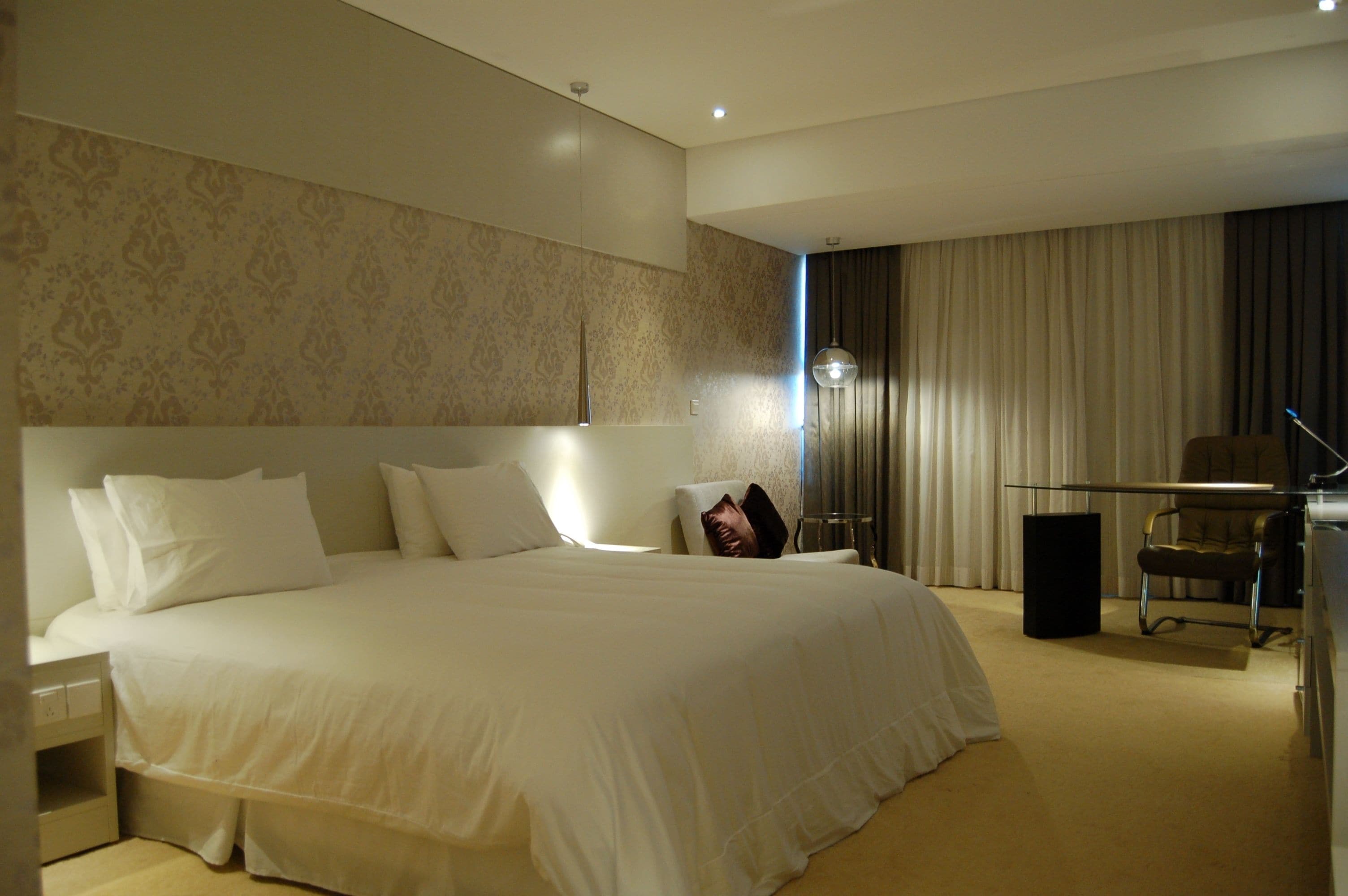A hotel room with a large bed, a desk with a chair, and a view of the outside through a window.