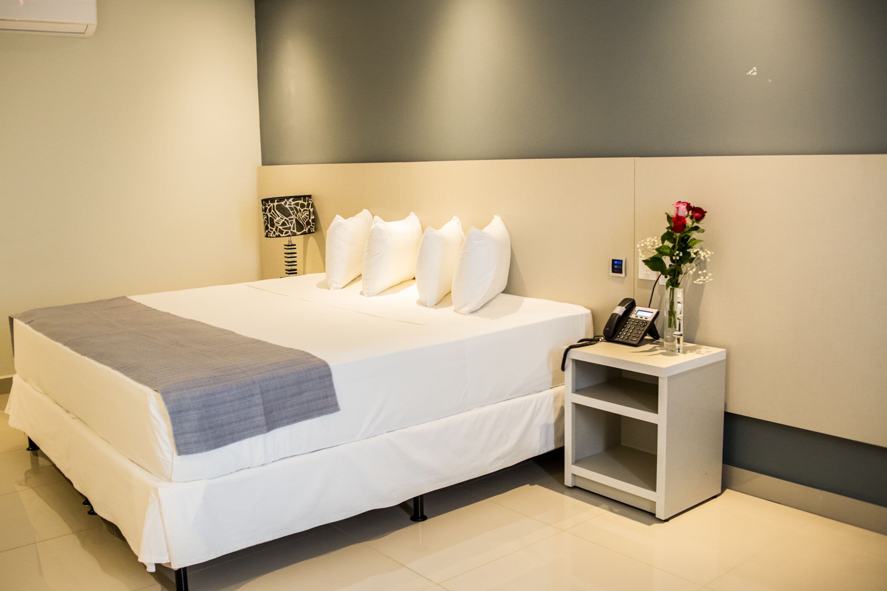 A neatly made bed with a gray blanket, a bedside phone, and a vase with flowers on a nightstand.