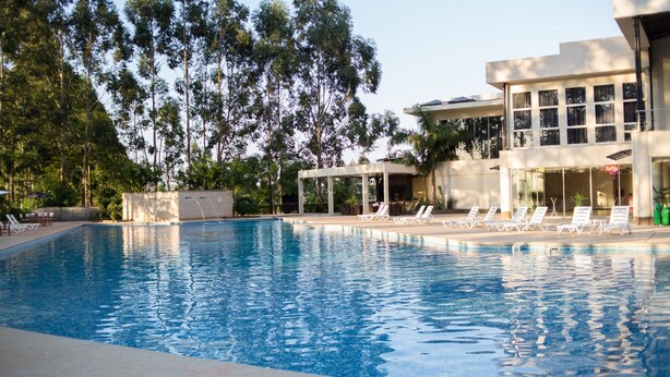 A swimming pool with lounge chairs and a covered seating area, surrounded by trees and a building with large windows. - Nobile Hotel Convention Ciudad Del Este (Ciudad Del Este)