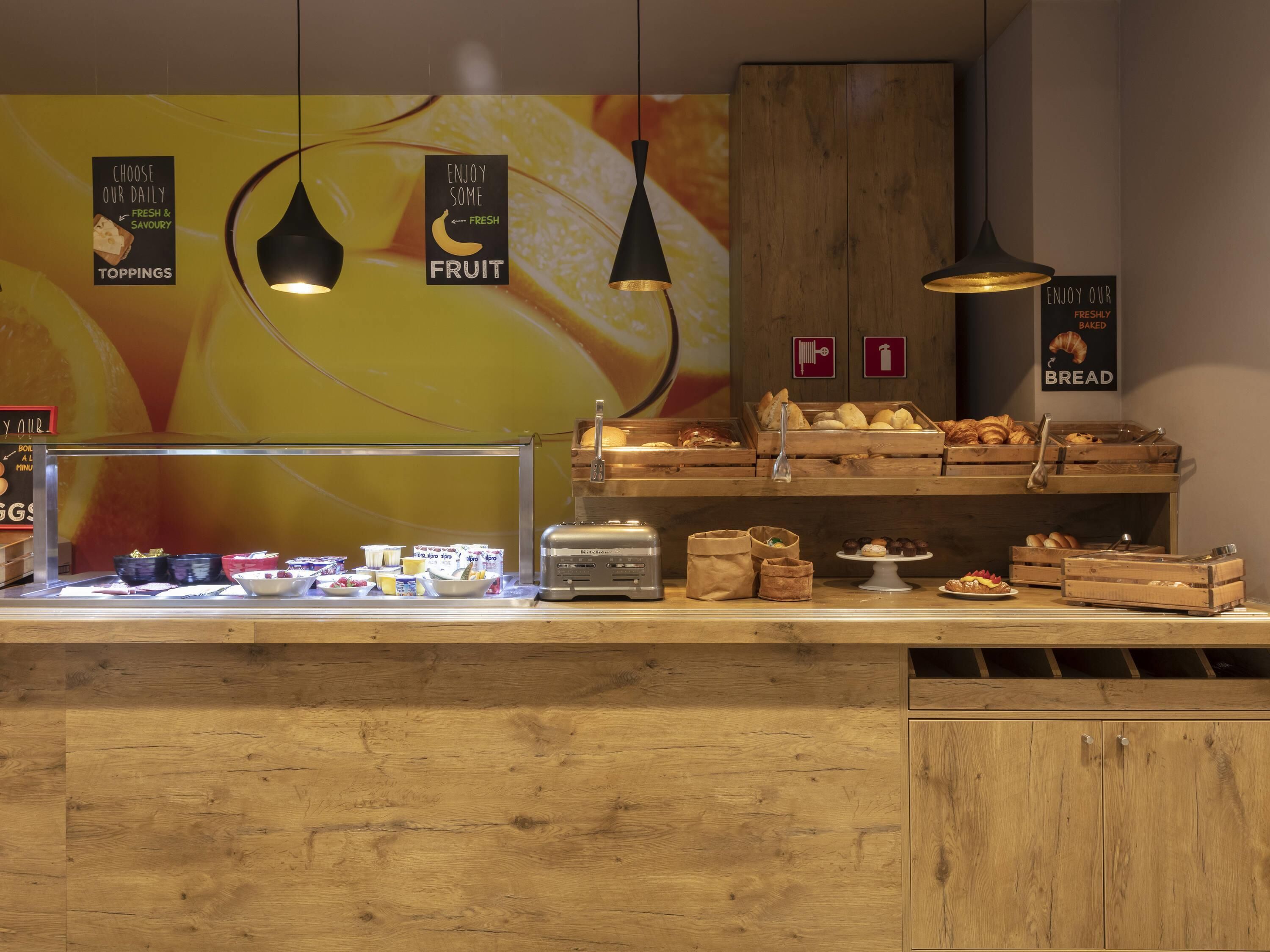 Ein Frühstücksbuffet mit verschiedenen Speisen und Schildern, die die Tagesauswahl wie frisches Obst und Backwaren zeigen.