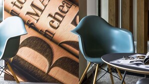 Un intérieur moderne avec un mur orné de motifs, deux chaises bleues et une petite table sur laquelle repose un magazine.