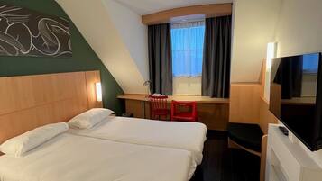 A hotel room with two beds, a desk, a chair, a TV, and a window with curtains.