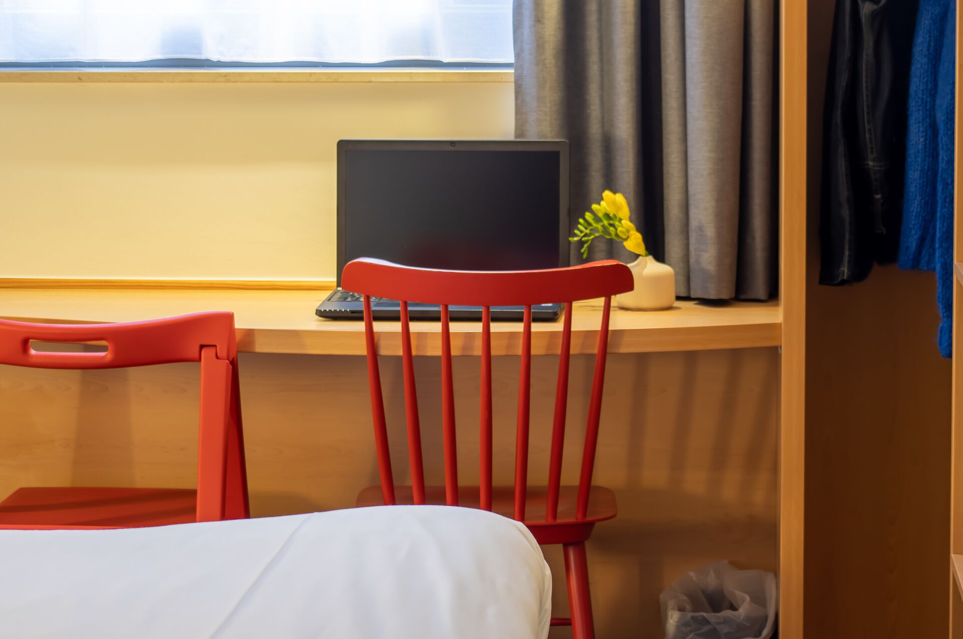 A room with a bed, a desk with a laptop, a chair, and a window with curtains.
