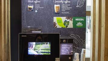 Uma estação de café Nescafé, com um ecrã de menu digital, uma máquina de café e um moedor de café.