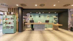 Un espace d’accueil comprenant un comptoir, une colonne en bois et une étagère verte où sont disposées des bouteilles.