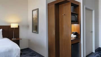 Een hotelkamer met een bed, nachtkastje, lamp, garderobe, magnetron en koelkast.