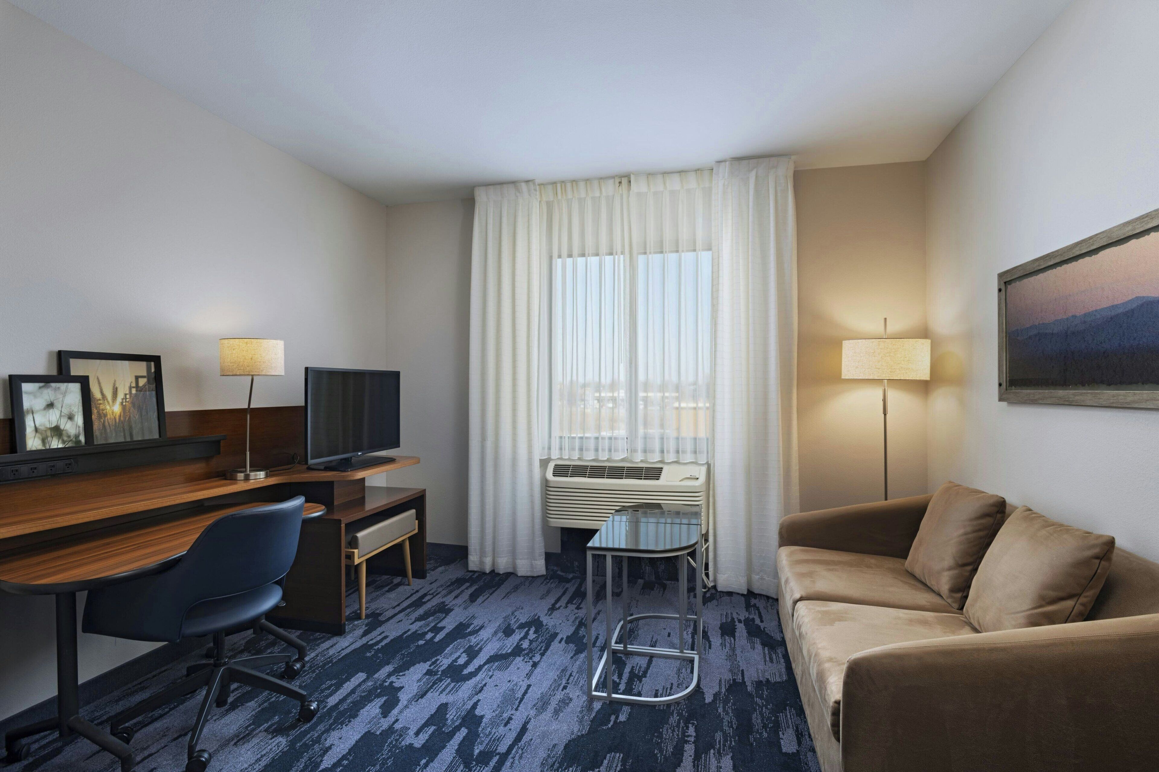 A hotel room with a desk, chair, sofa, and a TV.