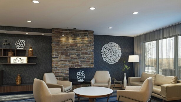 A modern lounge with leather sofas, a round coffee table, and a brick accent wall. - Fairfield Inn & Suites Des Moines Urbandale (Urbandale)