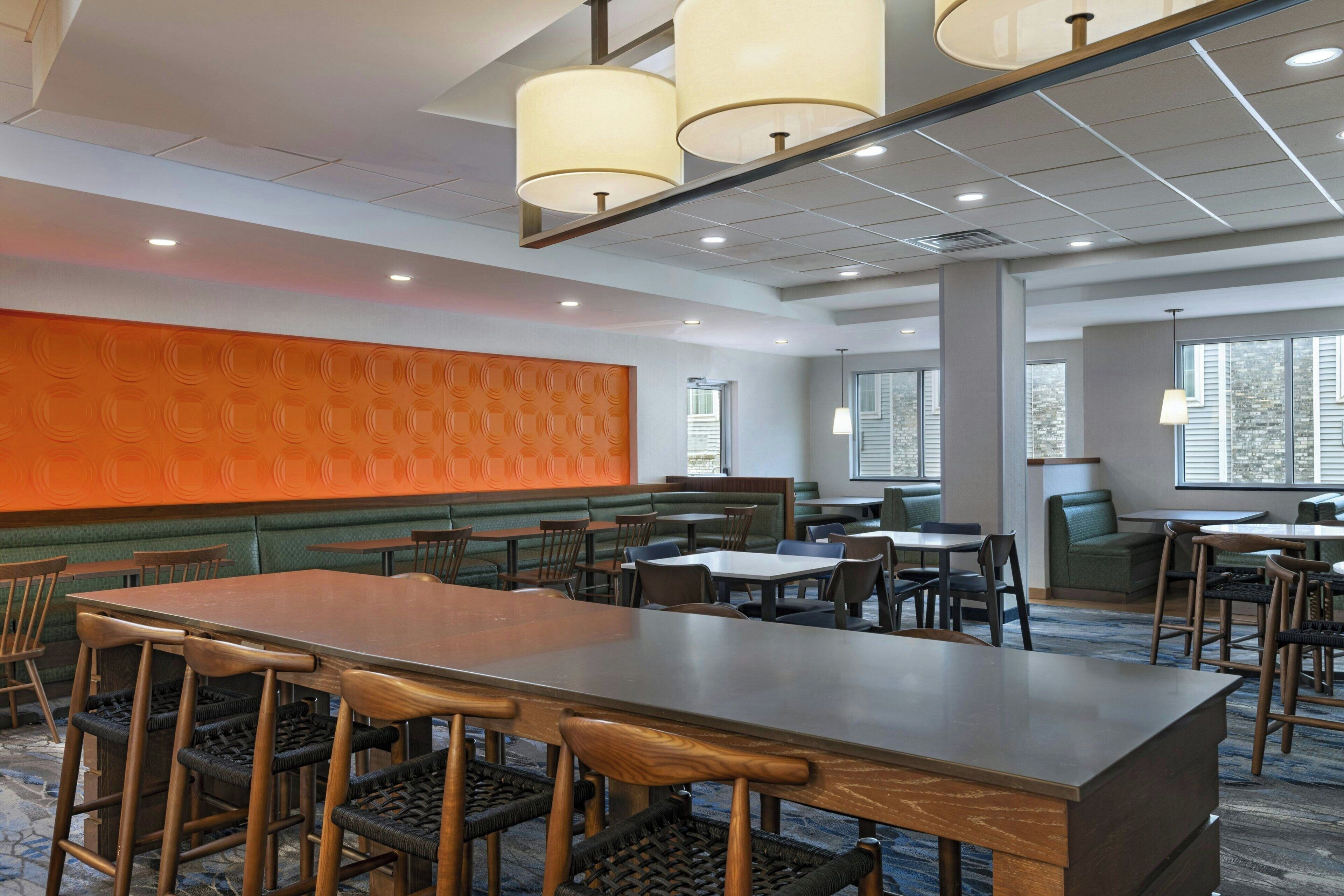 A hotel dining area with a long wooden table, multiple chairs, and a patterned wall.