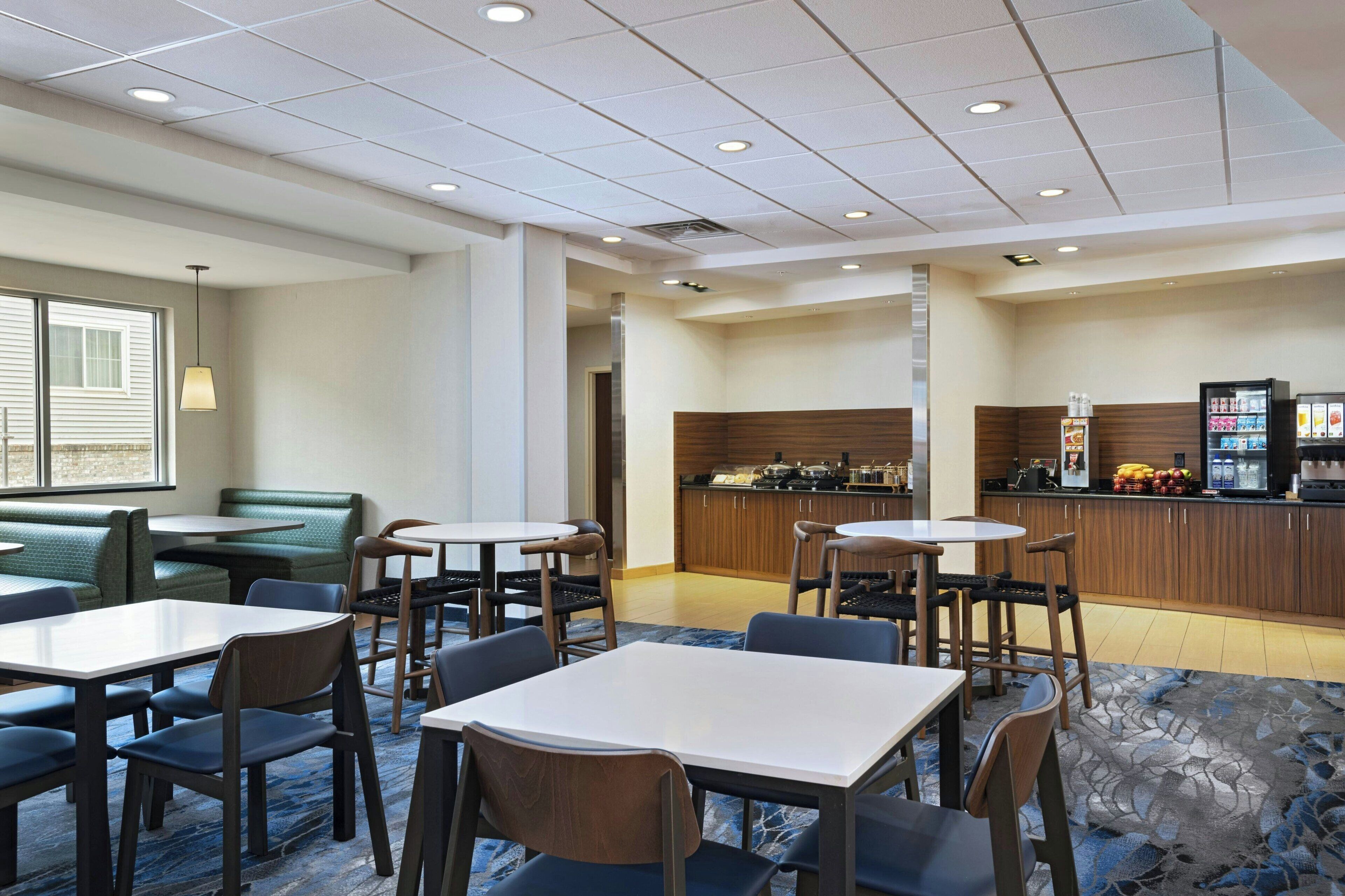 A hotel lobby with seating areas, a kitchenette, and a refrigerator stocked with beverages.