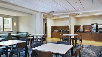 A hotel lobby with seating areas, a kitchenette, and a refrigerator stocked with beverages.
