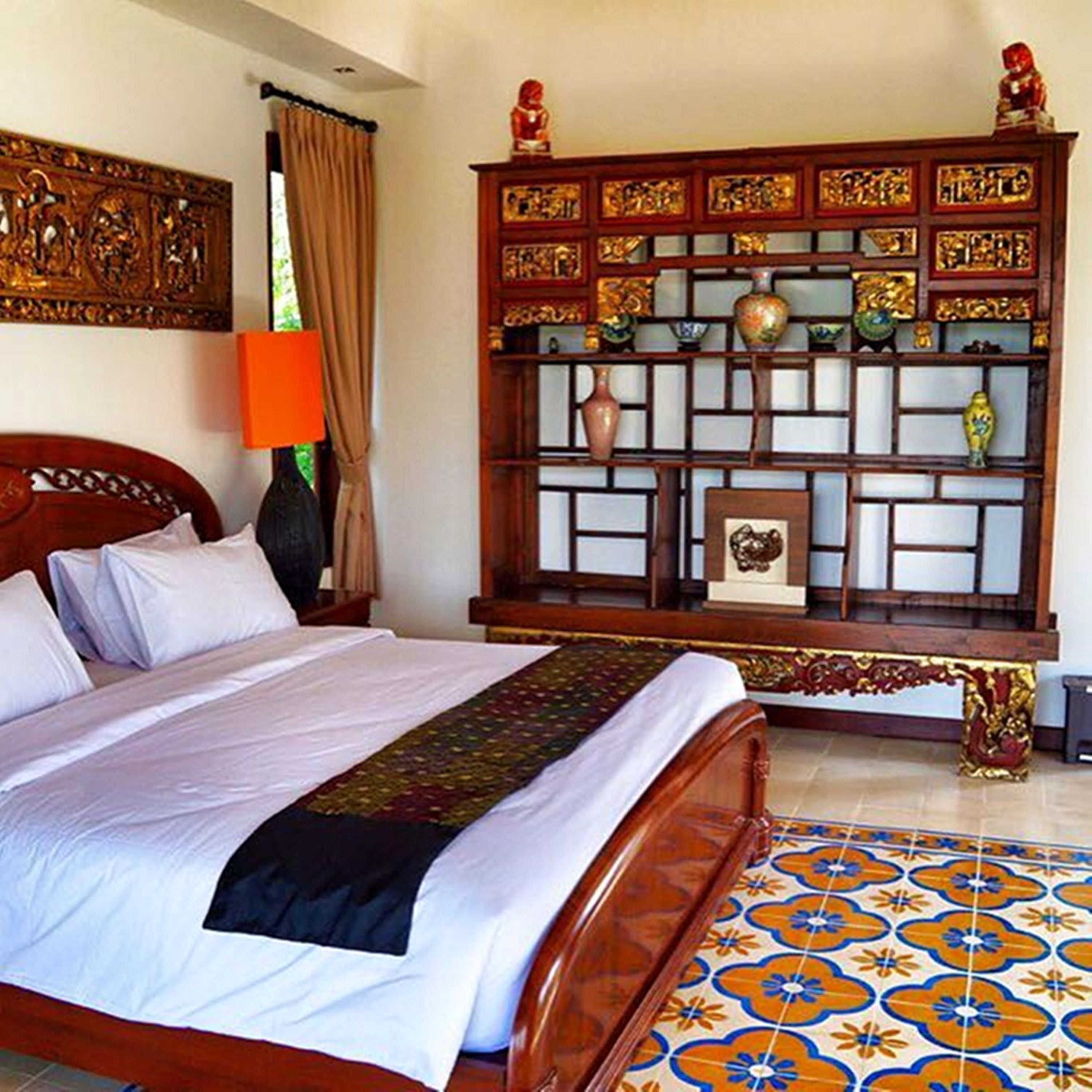 A neatly made bed with a patterned bedspread, a wooden nightstand with a lamp, and a decorative shelf with various items.