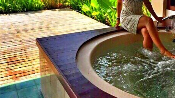 Una persona relajándose en un jacuzzi rodeado de abundante vegetación.