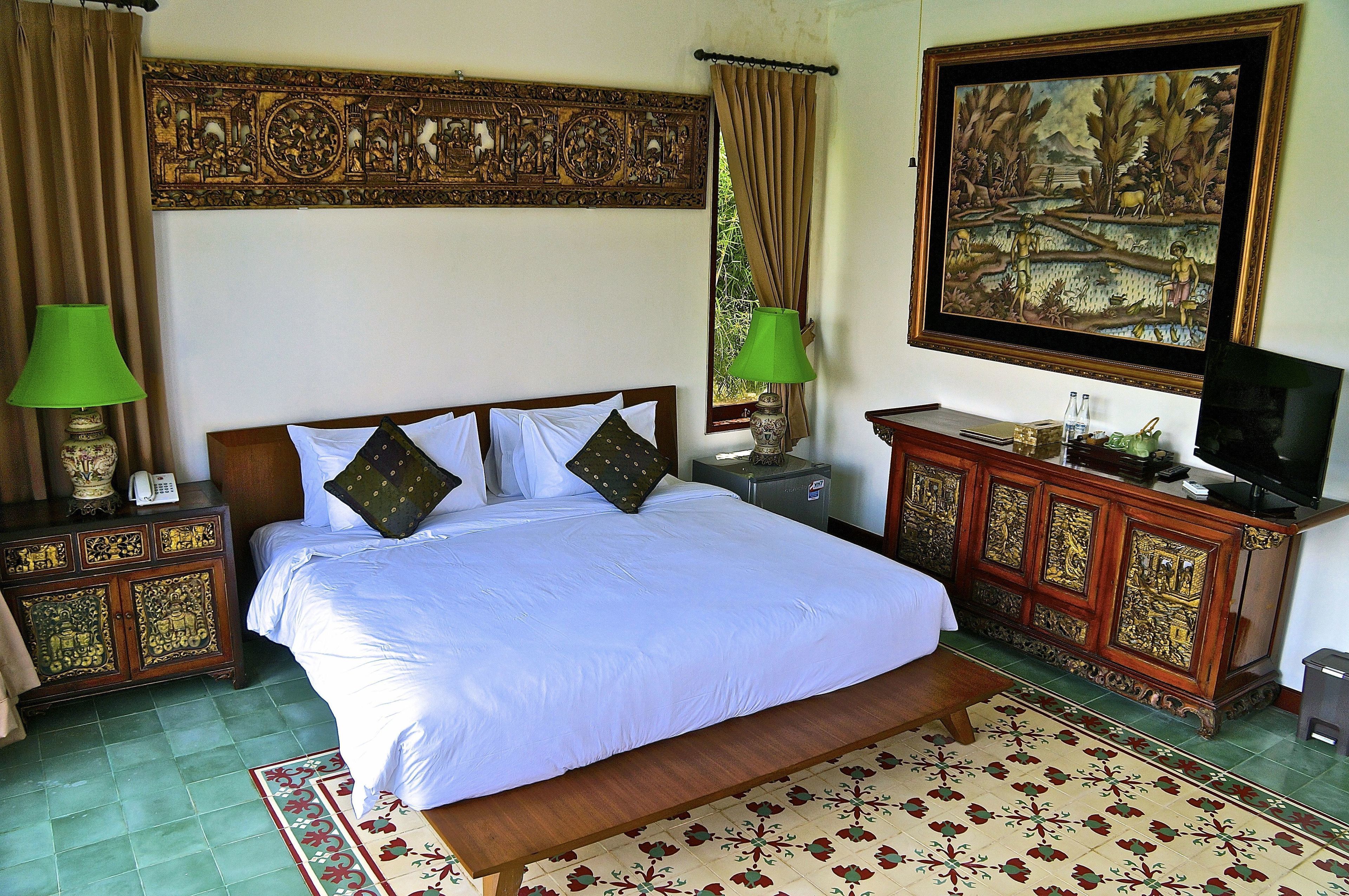 A bedroom with a large bed, two nightstands, a TV, and a decorative cabinet.