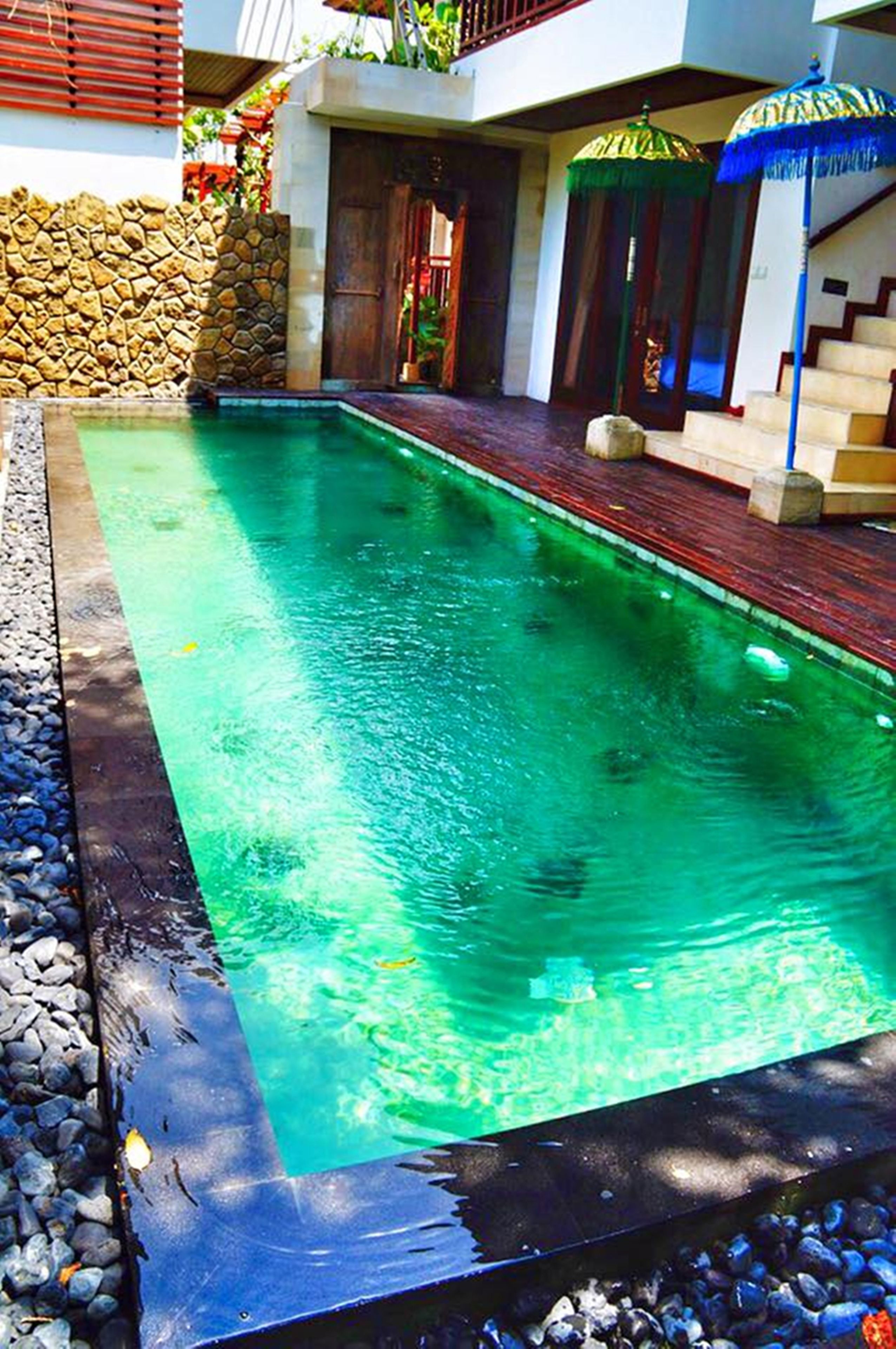 A rectangular swimming pool with a stone wall on one side and a wooden deck on the other.