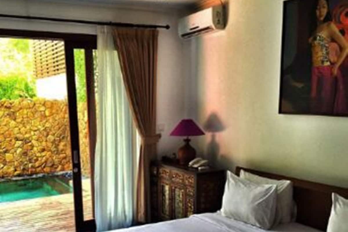 Habitación de hotel con cama, lámpara, cuadro y vista a una piscina.