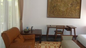 Una habitación con un sofá de cuero marrón, un escritorio de madera pequeño con una silla, una cama con colchón blanco y un cuadro grande en la pared.