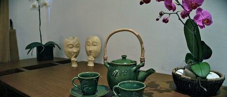 Una mesa de madera con una tetera verde, tazas a juego y una orquídea en maceta.