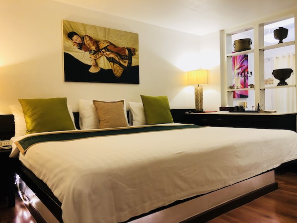 Quarto de hotel com uma cama grande, mesa de cabeceira, luminária e prateleira com objetos decorativos.