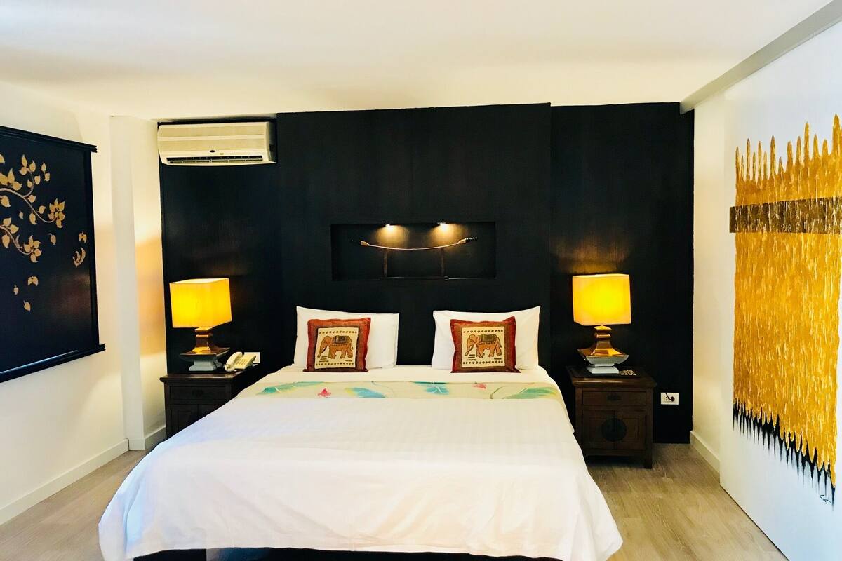 A hotel room with a large bed, two bedside tables, an air conditioning unit, and a wall-mounted TV.