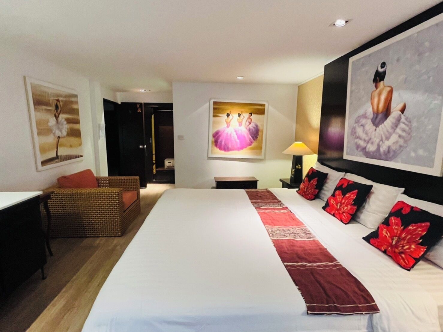 Una camera d'hotel con un letto grande, un'area relax con una poltrona in vimini e opere d'arte alle pareti.