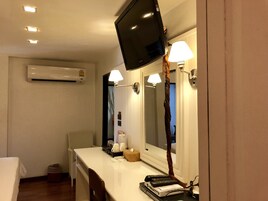 Habitación de hotel con cama, escritorio, televisor montado en la pared, espejo, lámpara y unidad de aire acondicionado.