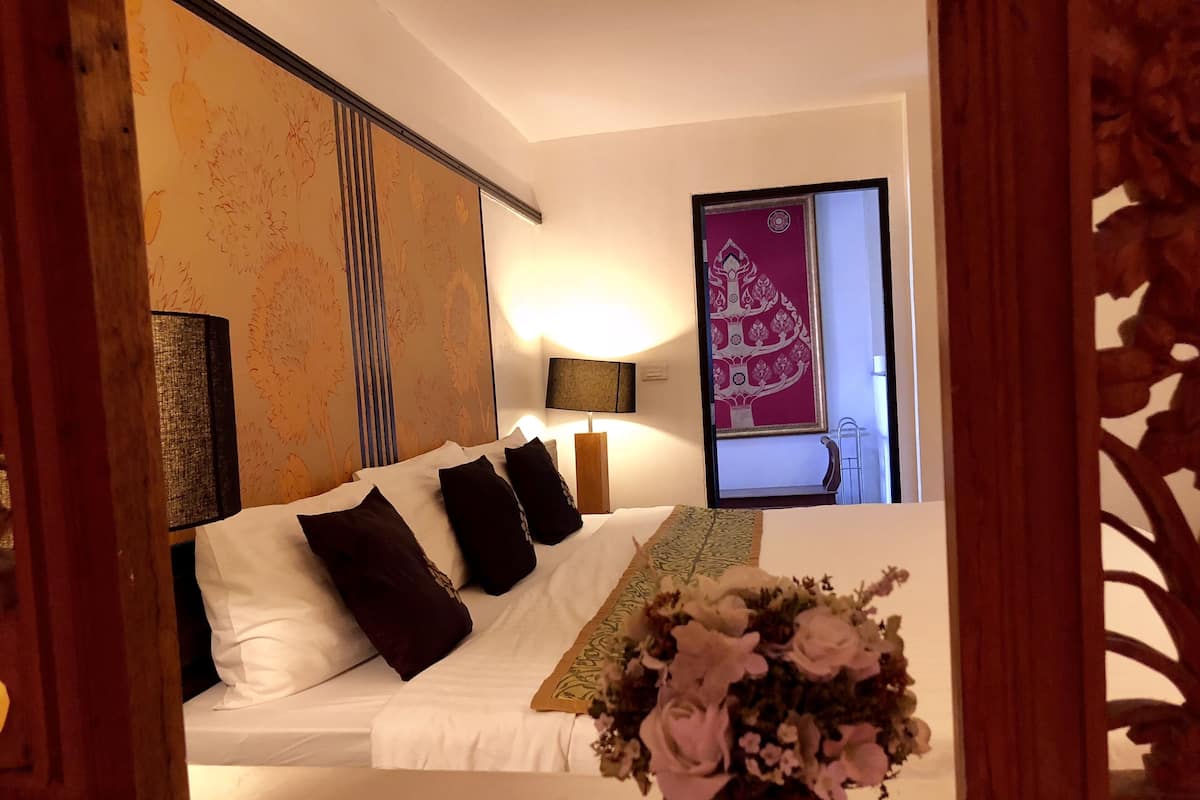 A hotel room with a bed, pillows, a bedside lamp, a floral arrangement, and a decorative wall panel.