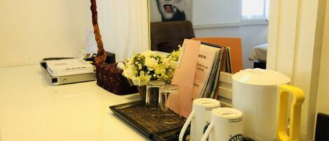 A desk with a printer, a decorative bag, a vase with flowers, a tray with Starbucks mugs, and a card holder with cards.