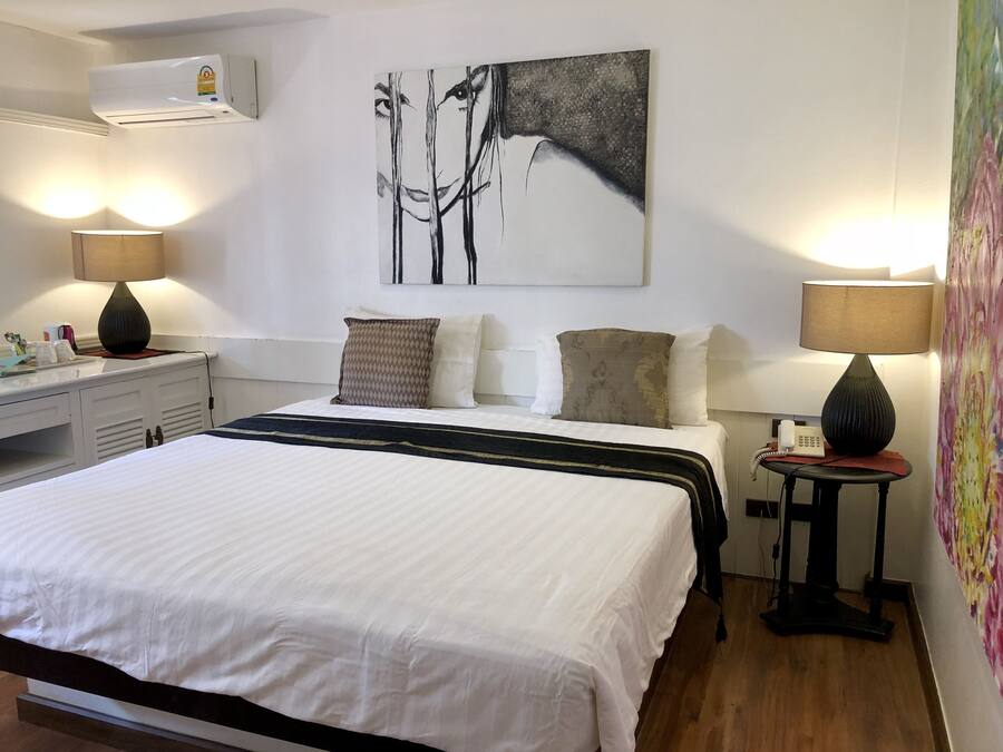 Habitación de hotel ordenada con una cama grande, dos lámparas de noche, aire acondicionado de pared y un cuadro sobre la cama.