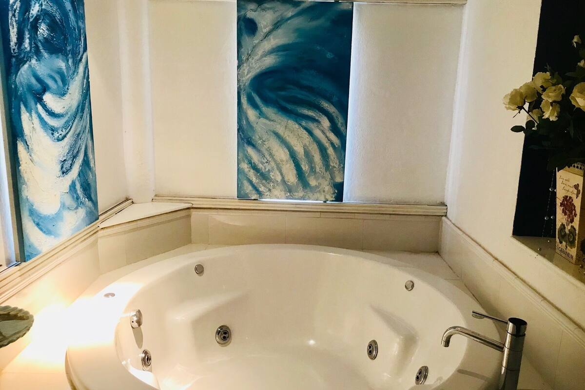 A bathroom with a freestanding bathtub, a window with a view, and a vase with flowers on the right.