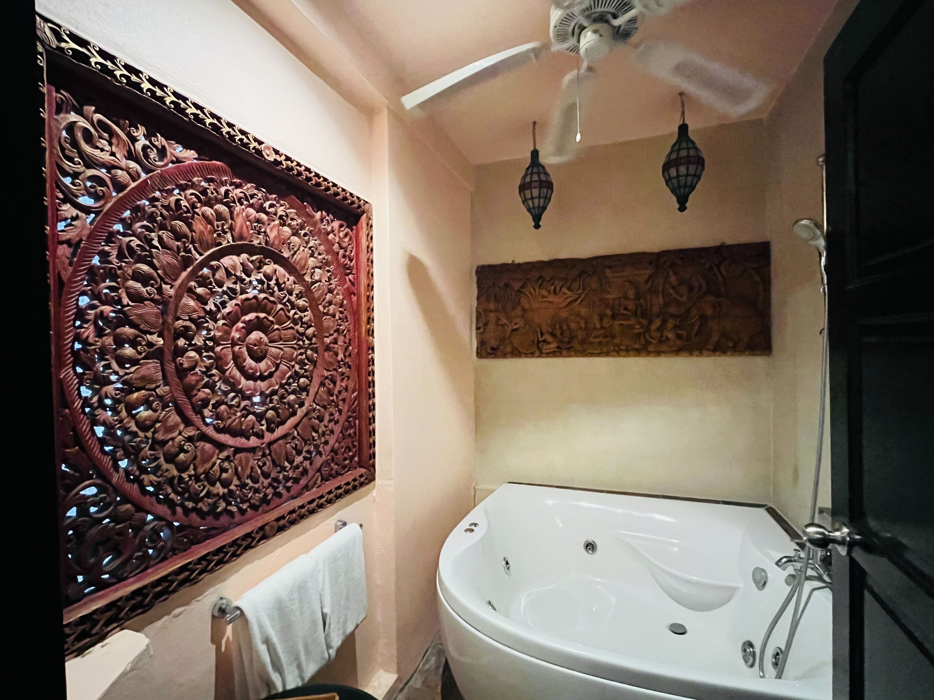 A bathroom with a decorative carved panel, a freestanding bathtub, and a ceiling fan.