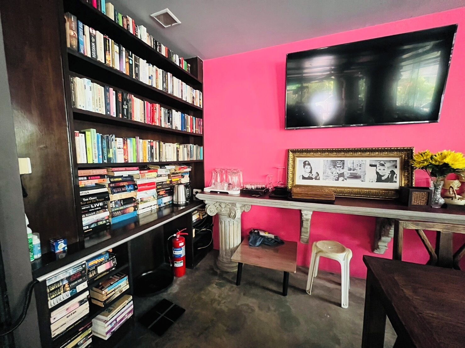 Ein Zimmer mit Bücherregal voller Bücher, einem an der Wand befestigten Fernseher, einem gerahmten Bild und einer Vase mit Blumen.