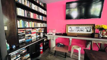 Ein Zimmer mit Bücherregal voller Bücher, einem an der Wand befestigten Fernseher, einem gerahmten Bild und einer Vase mit Blumen.