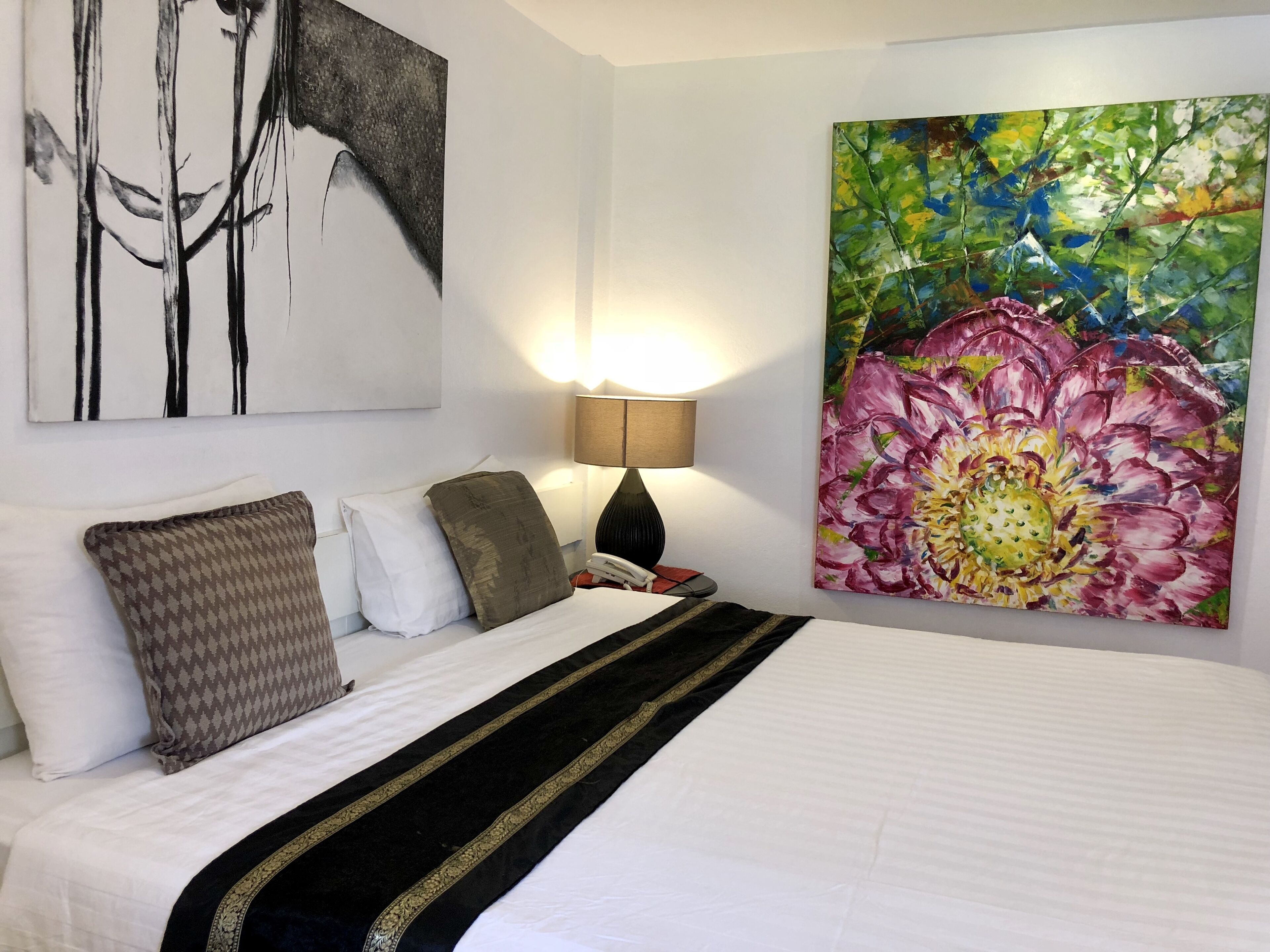 A hotel room with a large bed, a painting of abstract art, and a floral painting on the wall.