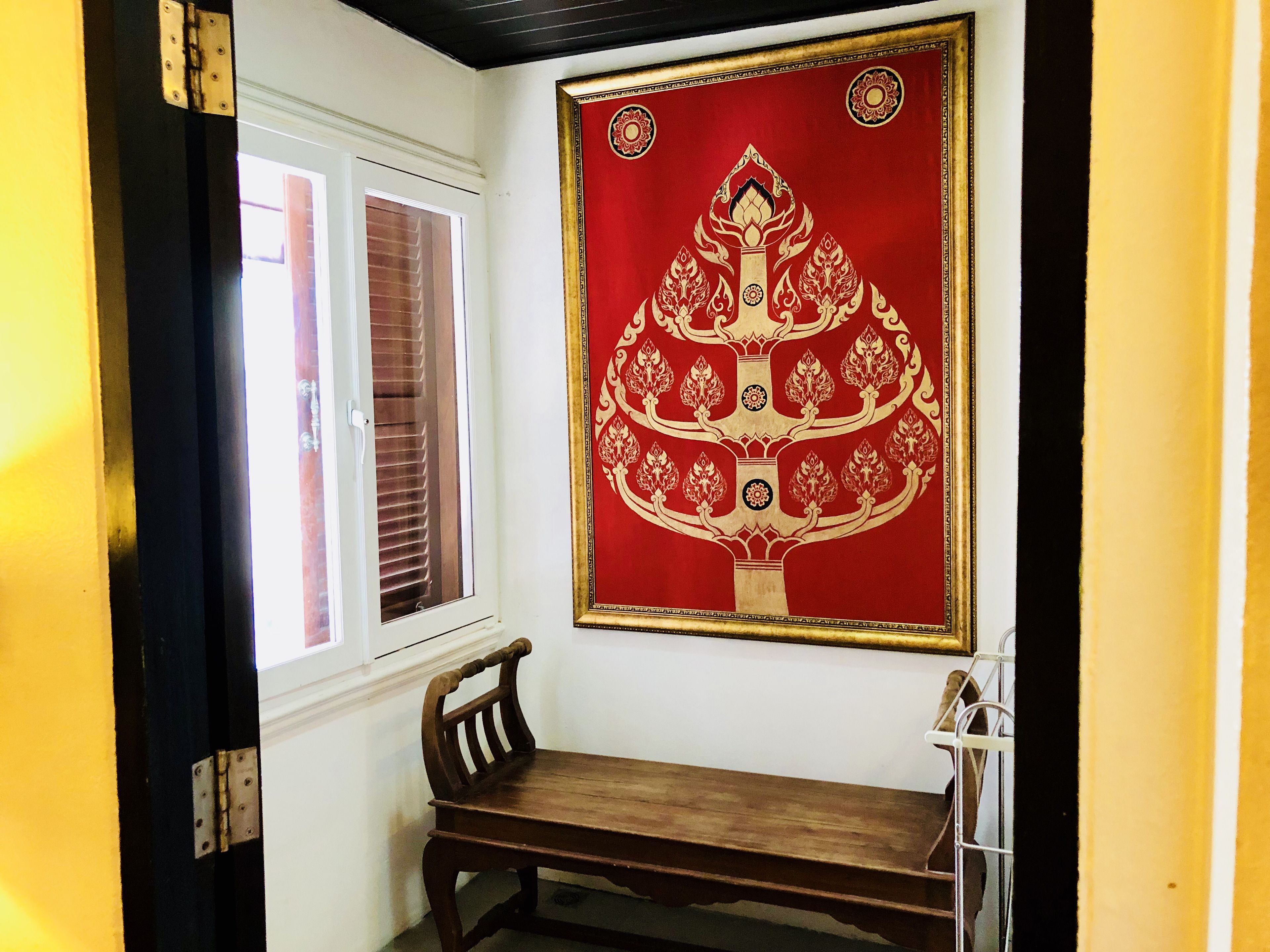 A room with a wooden bench, a window with blinds, and a red decorative wall hanging.